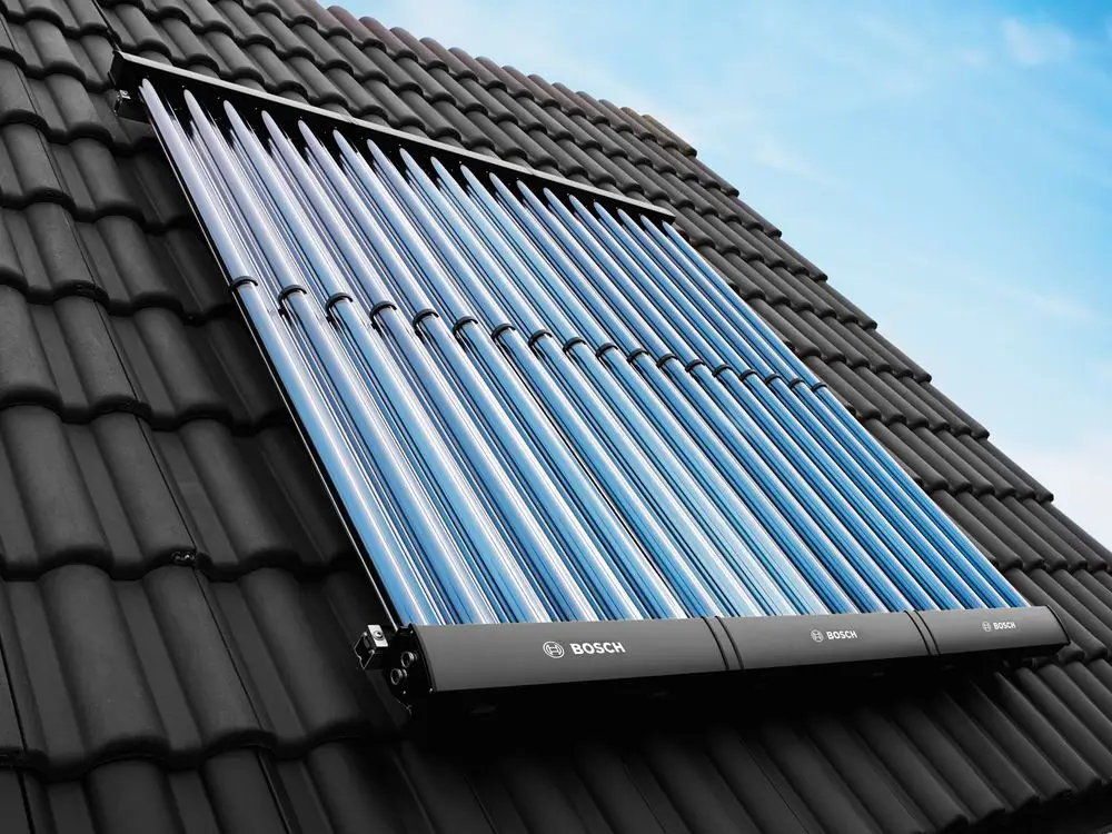Solar-Kollektor auf schwarzem Dach, bestehend aus mehreren blauen Röhren, zur Sonnenenergienutzung, mit Bosch-Logo sichtbar. Himmel im Hintergrund.